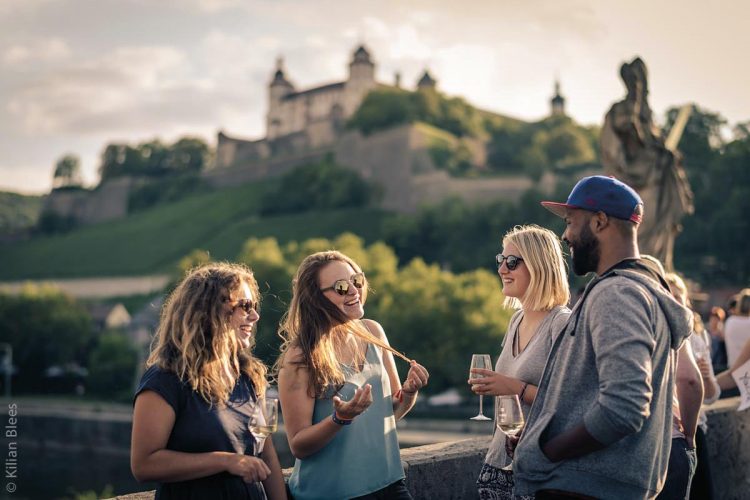 #wirfeiernbayern - Junge Menschen auf der Alten Mainbrücke in Würzburg, im Hintergrund die Festung Marienberg