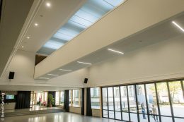 Eine Brücke verbindet im ersten Stock über der offenen Pausenhalle die beiden Gebäudeteile des Anbaus. Darüber befinden sich vier abgehängte Tageslichtelemente, die der Pausenhalle ein helles Ambiente verschaffen.