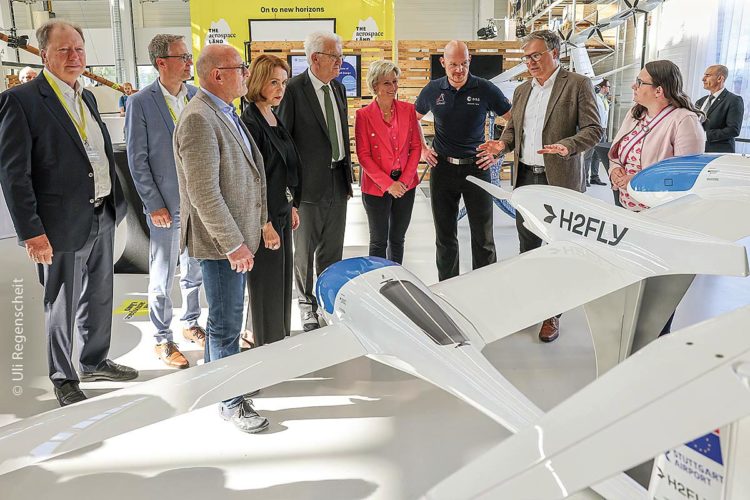 Ministerpräsident Winfried Kretschmann, ESA-Astronaut Alexander Gerst und weitere Teilnehmende stehen bei einem Rundgang an einem Modell des Forschungs- und Versuchsflugzeugs HY4.
